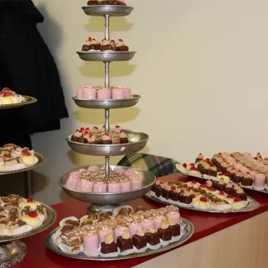 Ein Tisch ist mit verschiedenen Desserts wie Kuchen, Cupcakes und Gebäck auf Silberschalen und Tellern dekoriert. Ein dreistufiger Kuchenständer ist prominent ausgestellt und zeigt eine Auswahl an süßen Leckereien.