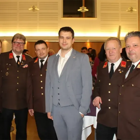 Fünf Männer in Uniformen, drei in Militäruniformen und zwei in Anzügen, stehen zusammen in einem Raum. Sie scheinen für ein Foto zu posieren.