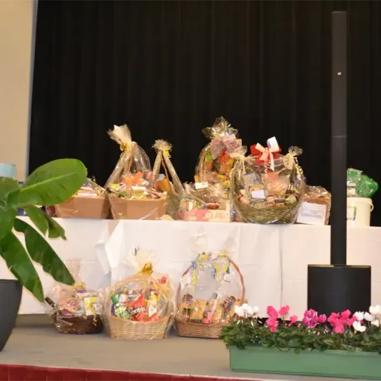 Ein Tisch mit verschiedenen Geschenkkörben und verpackten Artikeln zur Schau gestellt. Ein Lautsprecher steht neben dem Tisch. Ein Topf mit Pflanze und ein Blumenkasten sind im Vordergrund.