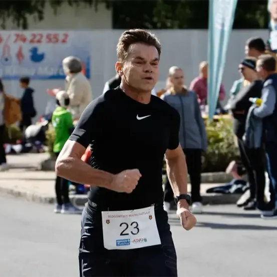 Ein Mann in einem schwarzen Nike-Shirt läuft bei einem Marathon mit der Nummer 23 auf seinem Startnummernband. Zuschauer beobachten ihn im Hintergrund.