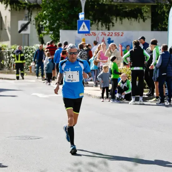 Ein Marathonläufer mit der Nummer 41 auf dem Trikot läuft auf einer Straße, an der eine Menschenmenge auf dem Bürgersteig steht.