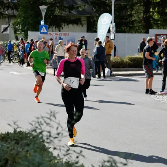 Zwei Läufer nehmen an einem Marathon teil, während Zuschauer die Straße säumen. Ein Läufer trägt ein grünes Shirt, der andere eine pinke und schwarze Kleidung.