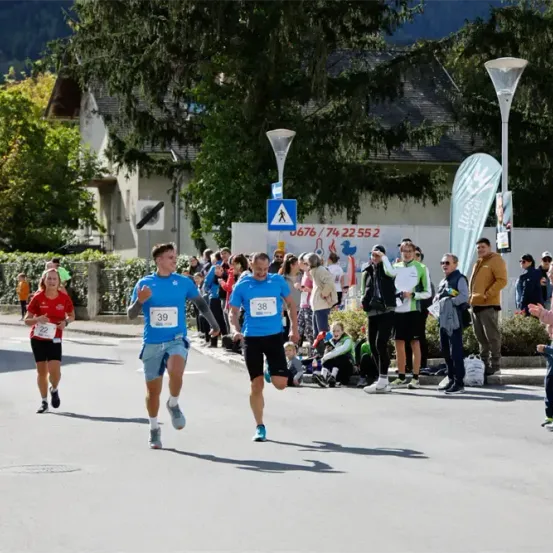 Läufer nehmen an einem Marathon teil, während Zuschauer sie anfeuern. Zwei Männer führen, einer mit der Nummer 39 und der andere mit 38. Eine Läuferin hinter ihnen trägt die Nummer 22.