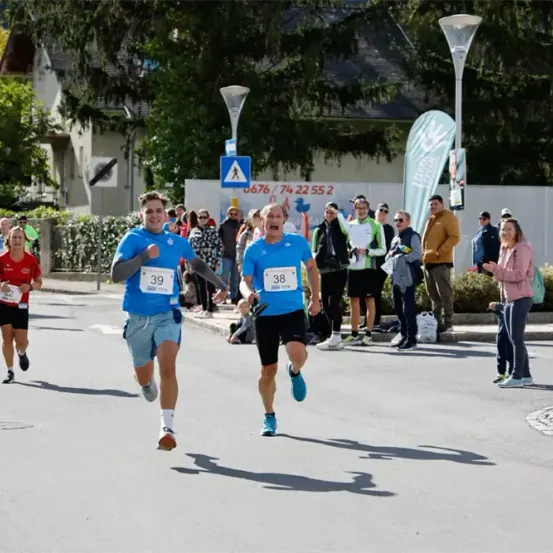 Zwei Läufer konkurrieren in einem Marathon, einer in Blau und der andere in Schwarz, mit Zuschauern an den Seitenlinien.