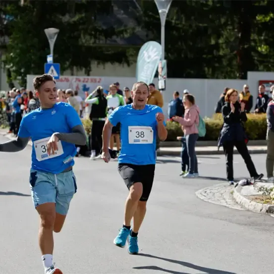 Zwei Männer laufen in einem Marathon. Einer trägt ein Shirt mit der Nummer 38, der andere mit 3. Dahinter jubeln Zuschauer.
