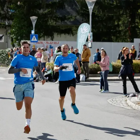 Zwei Männer laufen einen Marathon und tragen blaue Hemden und Shorts. Zuschauer feuern sie an.