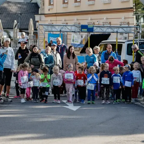 Eine Gruppe von Kindern, Erwachsenen und Zuschauern steht in der Straße, trägt nummerierte Startnummern und wartet wahrscheinlich auf einen Marathon.