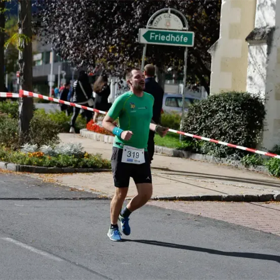 Ein Läufer mit der Nummer 319 läuft auf einer Straße mit einem grünen Straßenschild, das Friedhöfe besagt.