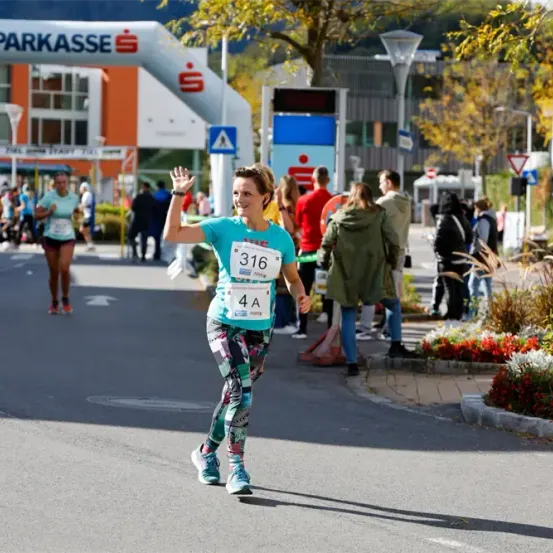 Eine Marathonläuferin winkt zur Kamera. Sie trägt ein Shirt mit der Nummer 316 und Leggings mit einem bunten Muster.