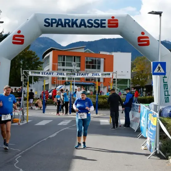 Marathonläufer laufen unter einem weißen Bogen mit dem Text 'Sparkasse'. Die Nummer 967 ist auf dem Shirt eines Läufers. Im Hintergrund befinden sich viele Menschen.