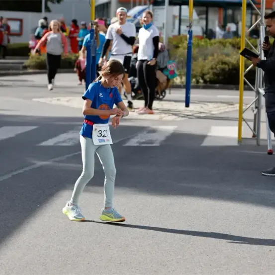 Ein kleines Mädchen mit der Nummer 32 auf ihrem Shirt läuft während eines Marathons in der Mitte der Straße.