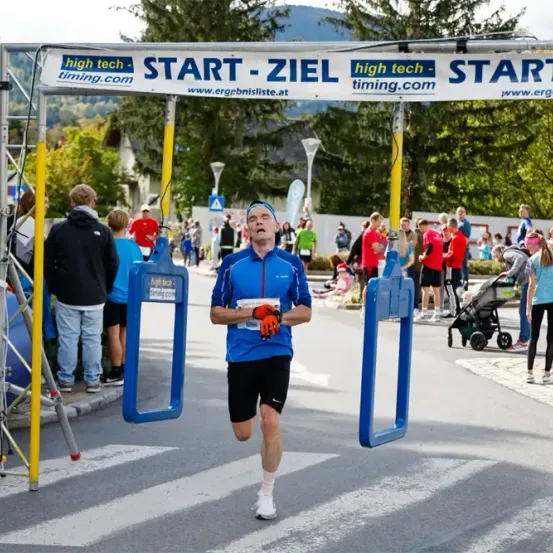 Ein Marathonläufer überquert die Ziellinie, während Zuschauer zuschauen, und ein Banner mit 'high tech timing.com' ist über ihm.