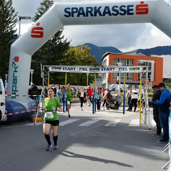 Ein Marathonläufer läuft durch den von Sparkasse gesponserten Zielbogen, mit Zuschauern und Schaulustigen, die ihn anfeuern.