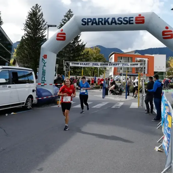 Läufer nehmen am Sparkasse-Marathon teil und passieren einen Start-Ziel-Bogen, mit einem geparkten Van in der Nähe.