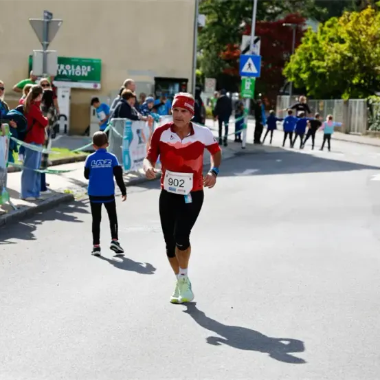 Ein Marathonläufer mit der Nummer 902 läuft auf der Straße, während Leute vom Bürgersteig zujubeln.