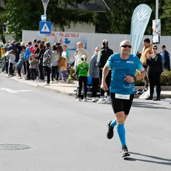 Ein Marathonläufer sprintet die Straße hinunter, während die Zuschauer vom Bürgersteig anfeuern. Ein Werbebanner ist an der Wand hinter den Läufern montiert.