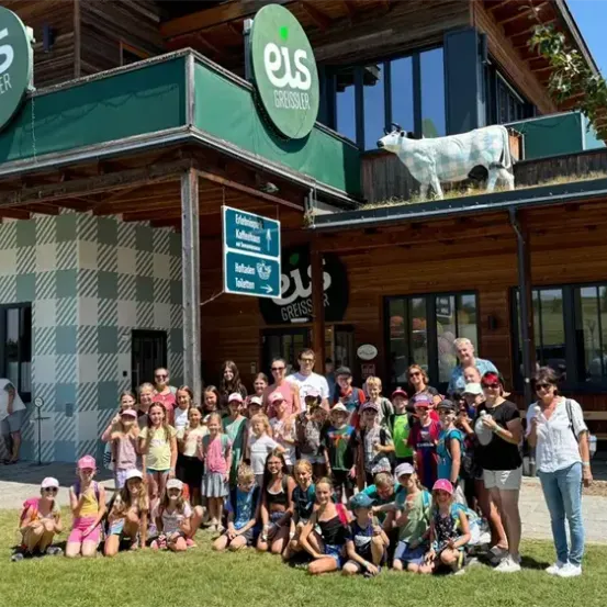 Eine Gruppe von Kindern und Erwachsenen steht vor einem Gebäude mit einer Kuh auf dem Dach und lächelt für ein Foto.
