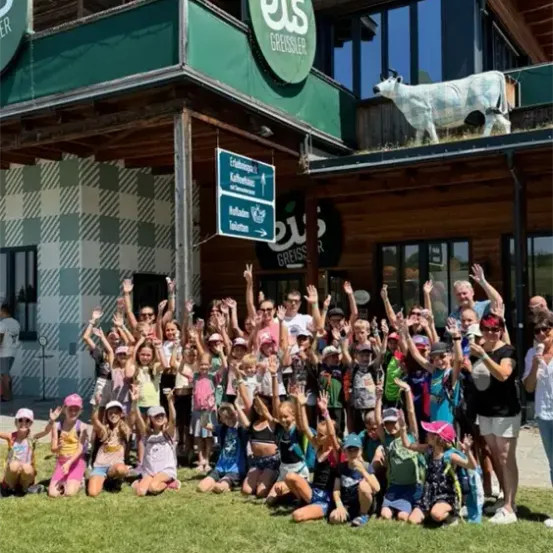 Eine Gruppe von Menschen posiert für ein Foto vor einem Gebäude mit dem Wort es darauf. Einige tragen Rucksäcke, Mützen und Brillen. Eine Kuhstatue befindet sich auf dem Dach.