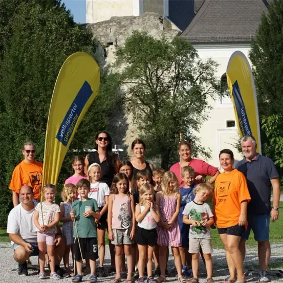 Eine Gruppe von Erwachsenen und Kindern posiert für ein Foto vor einem Gebäude mit Bannern im Hintergrund.