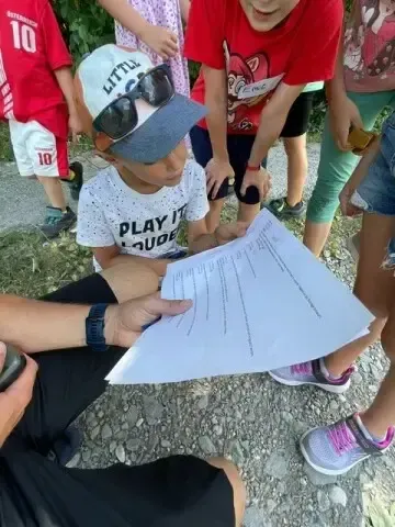 Ein junger Junge mit Hut und Sonnenbrille liest ein Stück Papier. Mehrere Kinder stehen hinter ihm.