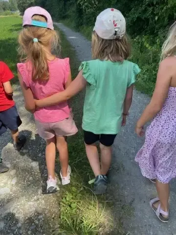 Vier Kinder, zwei Mädchen und zwei Jungen, gehen auf einem Schotterweg in einem grasigen Feld. Sie halten Händchen.
