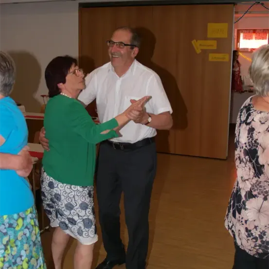 Ein älteres Paar tanzt mit zwei anderen Frauen in einem Raum mit Holzwänden und gelben Haftnotizen.