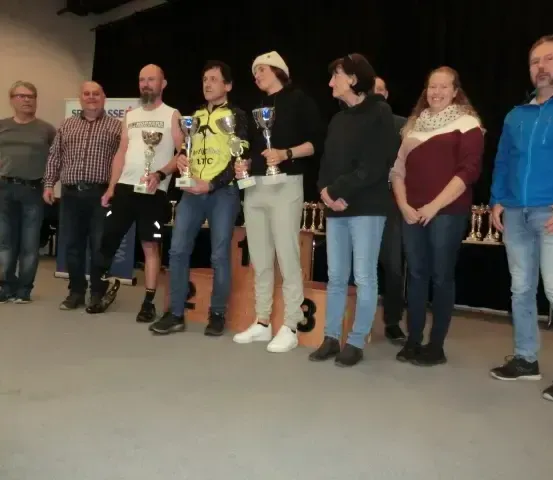 Eine Gruppe von Menschen steht auf einer Bühne, lächelt und posiert für ein Foto mit Trophäen in den Händen. Dahinter ist ein schwarzer Hintergrund.