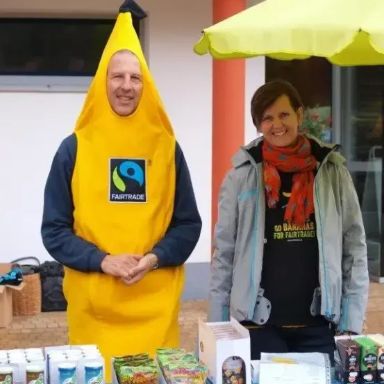 Ein Mann in einer Bananen-Kostüm und eine Frau in einer Jacke stehen an einem Tisch mit verschiedenen Artikeln.