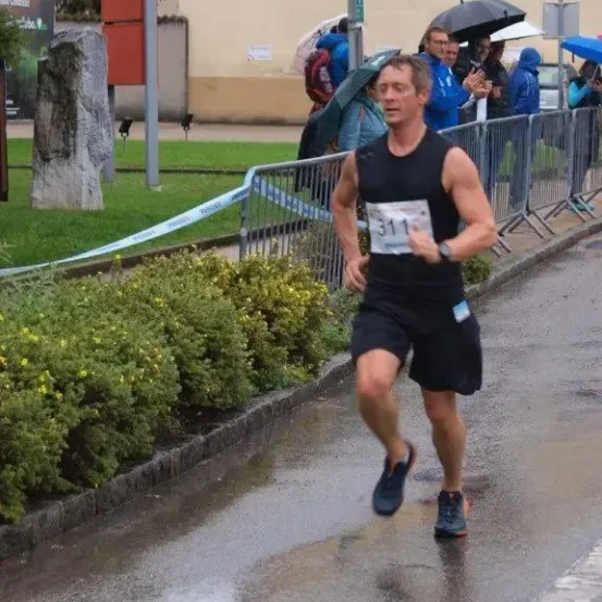 Ein Mann läuft einen Marathon, Nummer 311 auf seinem Shirt, mit Zuschauern und Regen.