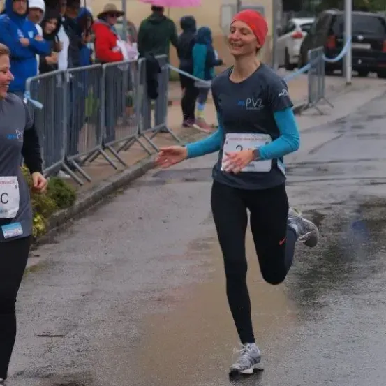 Eine Marathonläuferin lächelt, während sie im Regen läuft, mit einer weiteren Läuferin und Zuschauern in der Nähe.