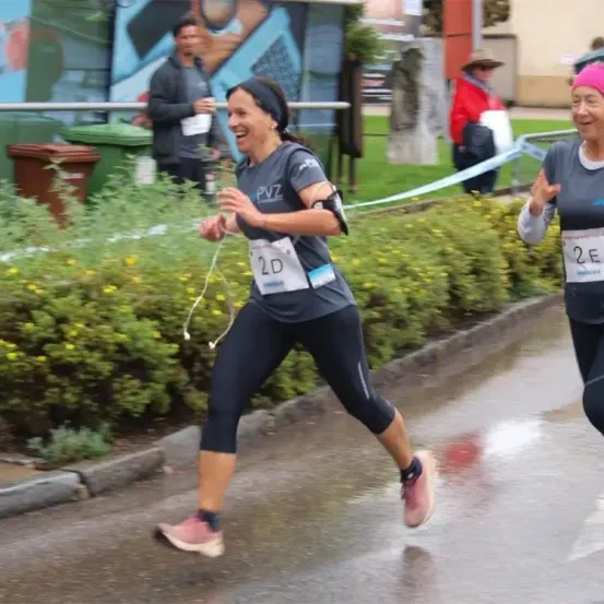 Eine Frau beim Marathon, die ein graues Shirt mit 2D trägt, läuft lächelnd auf einer nassen Straße.