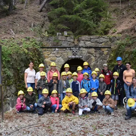 Eine Gruppe von Erwachsenen und Kindern, die Helme tragen, posiert für ein Foto vor einem Mineneingang.