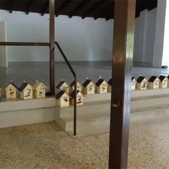 Ein Raum mit einer weißen Wand, einer Tür und einer Treppe. Viele kleine Vogelhäuschen sind auf der Treppe aufgereiht.