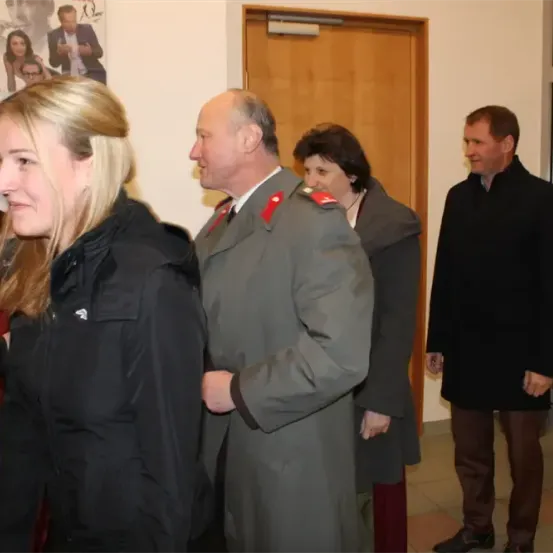 Eine Gruppe von Menschen, darunter eine Frau und ein Mann in Uniform, steht in einem Flur und unterhält sich.