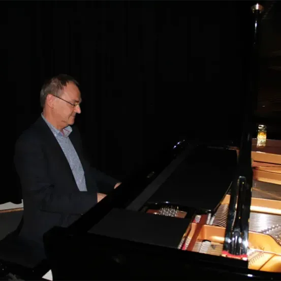 Ein Mann mit Brille und Anzug sitzt lächelnd an einem Flügel. Die Deckel des Klaviers sind geöffnet und die Saiten sind sichtbar.