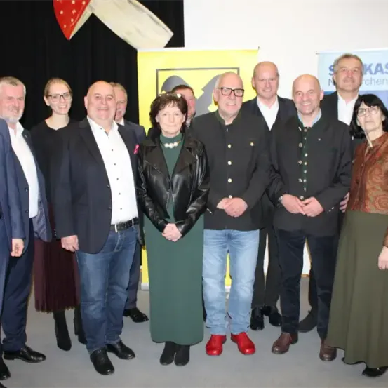 Eine Gruppe von Menschen steht vor einem gelben Banner. Sie tragen formelle Kleidung. Einige lächeln und andere schauen in die Kamera. Der Mann in der Mitte trägt einen roten Schuh.