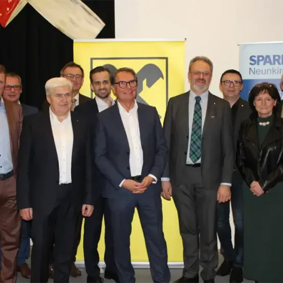 Eine Gruppe formell gekleideter Personen steht für ein Foto vor einem gelben Banner mit einem Logo und einem SPARKA Neunkirchen-Banner.