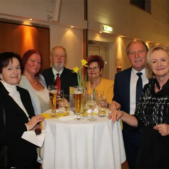 Eine Gruppe von Erwachsenen lächelt und posiert für ein Foto bei einer Veranstaltung mit Getränken auf einem Tisch.