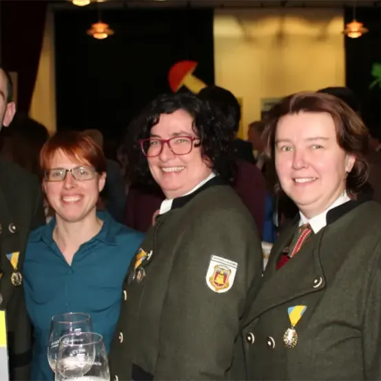 Vier lächelnde Personen posieren für ein Foto. Ein Mann und zwei Frauen in Uniformen mit Abzeichen und Medaillen. Die Frau links hält ein gelbes Plakat.