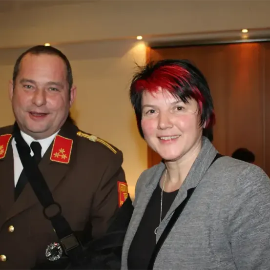Ein Mann in einer Militäruniform mit Sternen auf den Schultern steht neben einer Frau mit roten Haaren, beide lächeln für ein Foto.