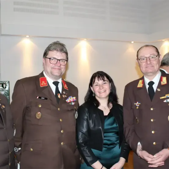 Vier Menschen in Uniformen, darunter eine Frau, stehen in einem Raum mit weißen Wänden und Deckenleuchten.