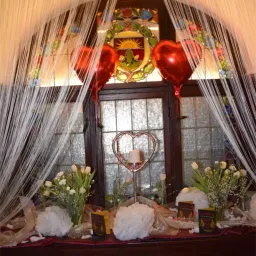 Eine dekorative Ausstellung mit roten Herzballons und weißen Blumen vor einem Buntglasfenster.