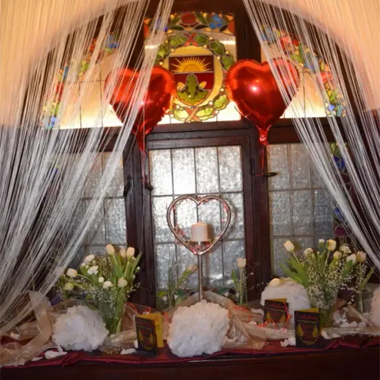 Eine dekorative Ausstellung mit roten Herzballons und weißen Blumen vor einem Buntglasfenster.