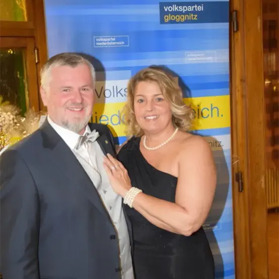 Ein Mann und eine Frau stehen eng beieinander vor einem blau-weißen Banner mit Text.