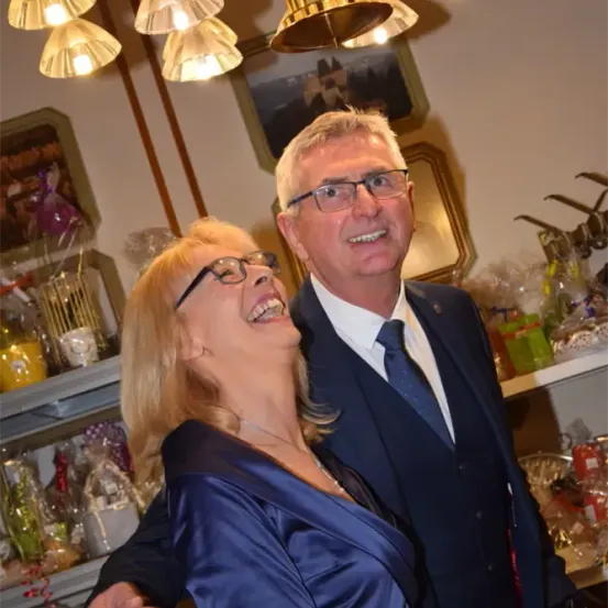 Ein Mann und eine Frau stehen lächelnd vor einem Geschäft voller Geschenke und Dekorationen, mit einer Kronleuchter, die von der Decke hängt.