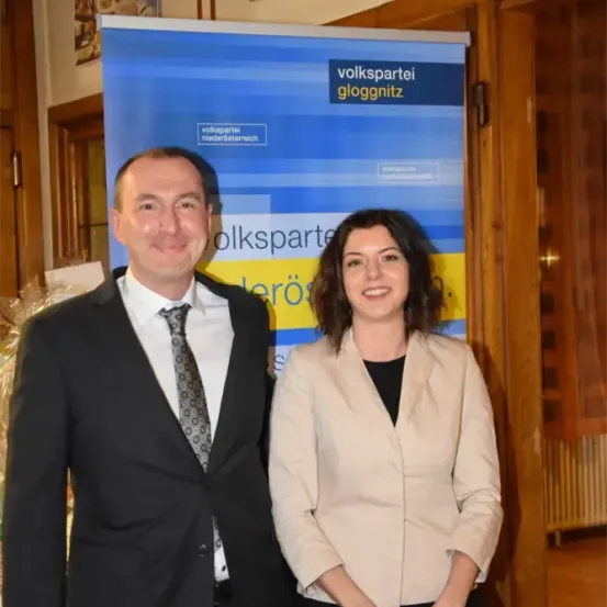 Ein Mann und eine Frau stehen lächelnd vor einem Volkspartei Niederosterreich-Banner.