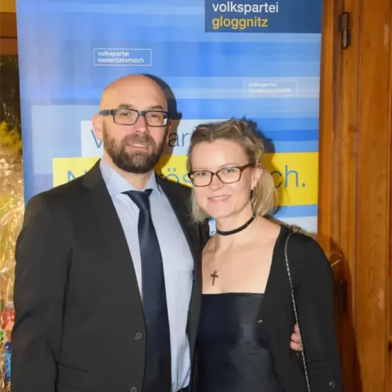 Ein Mann und eine Frau stehen gemeinsam vor einem Volkspartei Niederosterreisch-Banner. Der Mann trägt einen Anzug und eine Krawatte, und die Frau trägt ein schwarzes Kleid und eine Brille.