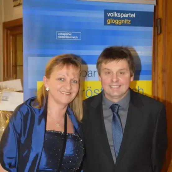 Eine Frau und ein Mann stehen nebeneinander und lächeln für die Kamera vor einem blau-gelben Banner mit dem Text 'volkspartei gloggnitz'.