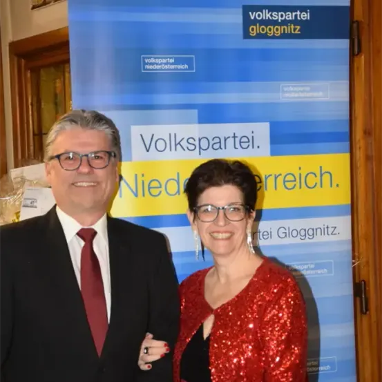 Ein Mann und eine Frau stehen vor einem Volkspartei Niederosterreich-Banner. Sie lächeln beide und tragen formelle Kleidung.