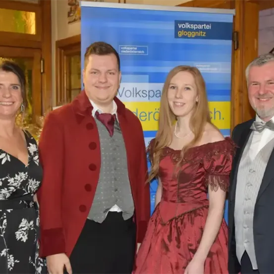 Vier Menschen stehen eng beieinander vor einem Banner, das Volkspartei sagt. Ein Mann und eine Frau sind in historischer Kleidung gekleidet, während die anderen zwei formelle Kleidung tragen.